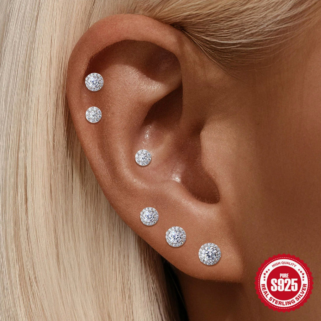 Close-up of an ear wearing multiple silver earrings with a '925 Sterling Silver' stamp.