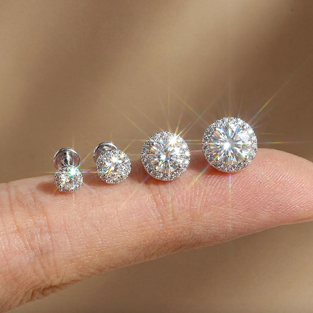 Four diamond stud earrings displayed on a finger against a neutral background